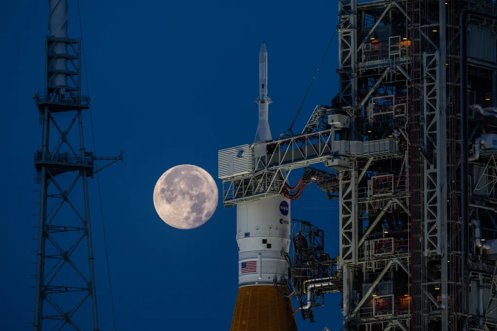 Photo de la fusée SLS de nuit,, avec la pleine lune en toile de fond (programme Artemis 2026).